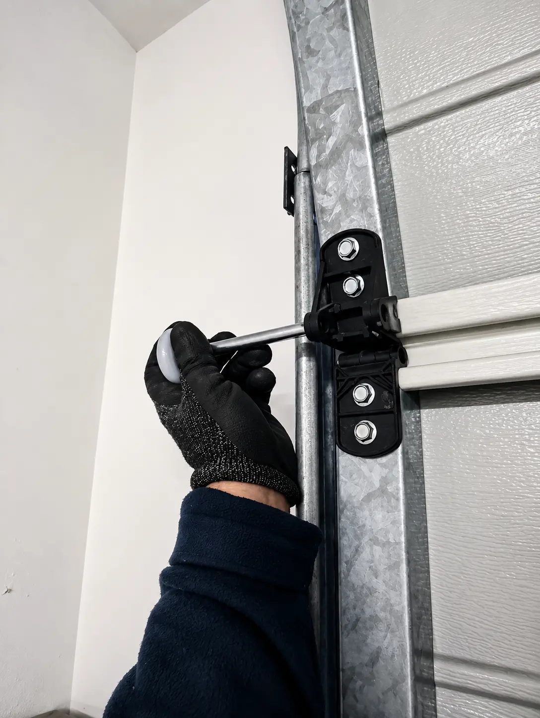 Technician tightening garage door hinge hardware during a repair